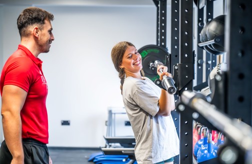 Sports student placing a barbell back on the rack, smiling