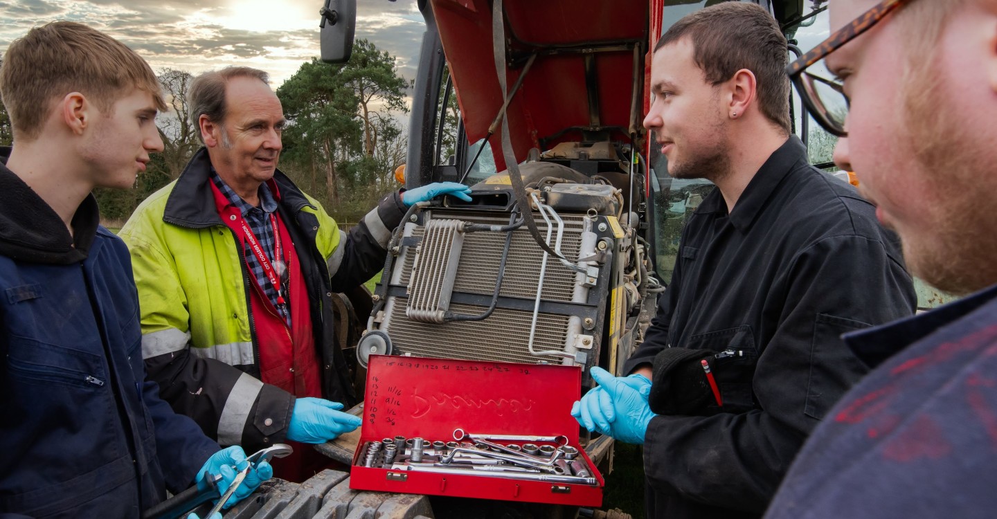 Agriculture Engineering students working on a tractor in the field with their lecturer