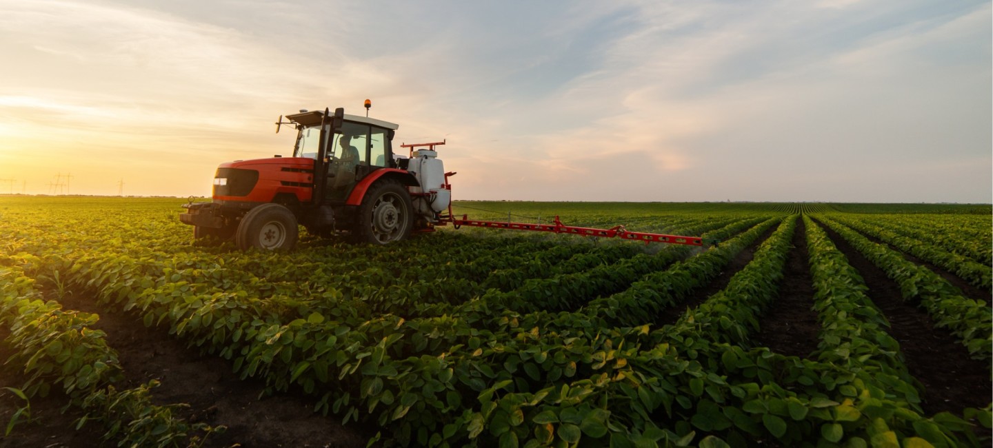 Farmer in tractor fertilising a field at sunset