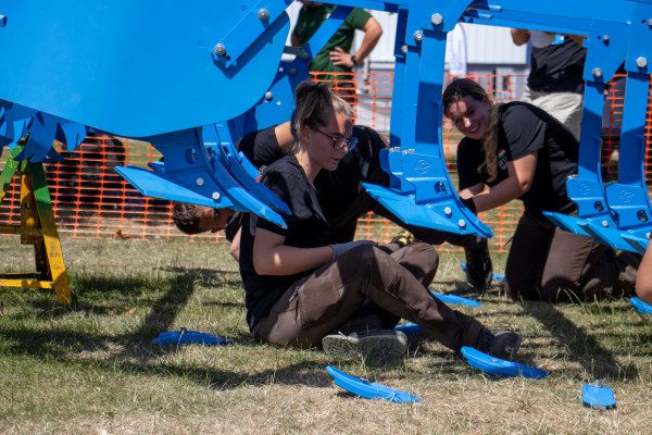 Students sitting on the ground and changing the points on a blue cultivator