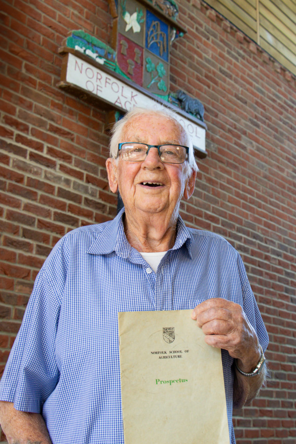 James Medler with the 1953 prospectus standing in front of the old Norfolk School of Agriculture sign.