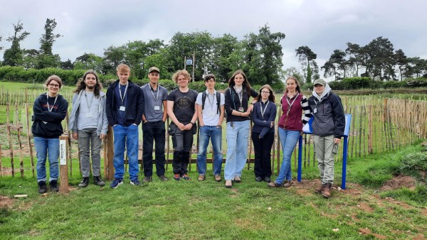 A group picture of 10 students in front of a fenced area where saplings have been planted